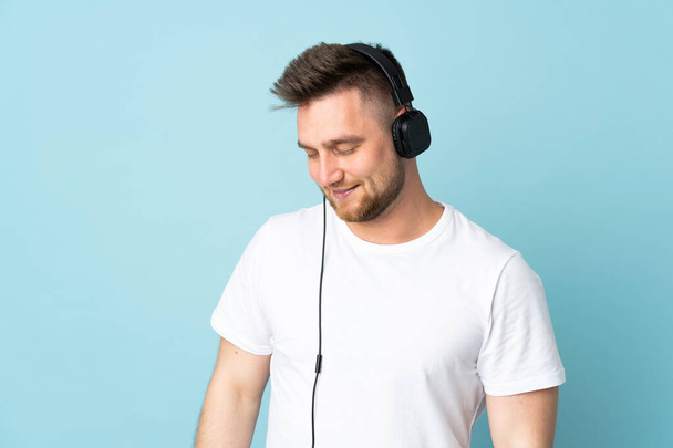 Russisch schöner Mann isoliert auf blauem Hintergrund Musik hören - Foto, Bild