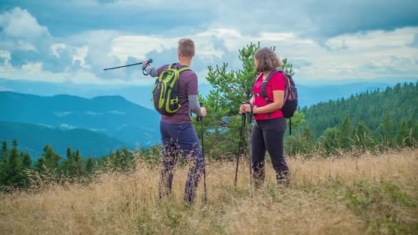 Nuori retkeilijä pari ihaillen kaunis näkymä vuorille saavuttaessaan huippu Ribnica Na Pohorju, Slovenia pilvinen päivä. - Materiaali, video