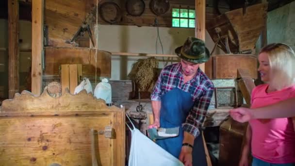 Molinero anciano muestra a potenciales clientes jóvenes la muestra de su grano producido en un saco, molino de Povhov - Imágenes, Vídeo