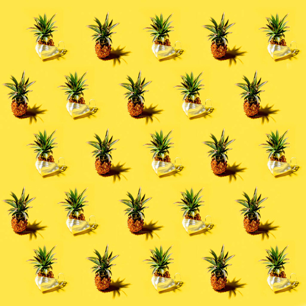 Fresh mini pineapples ananases and pineapples in medicine respirator mask with shadows on a bright solid yellow background pattern. Tropical style, summer pandemic vacation or illness concept. - Foto, imagen