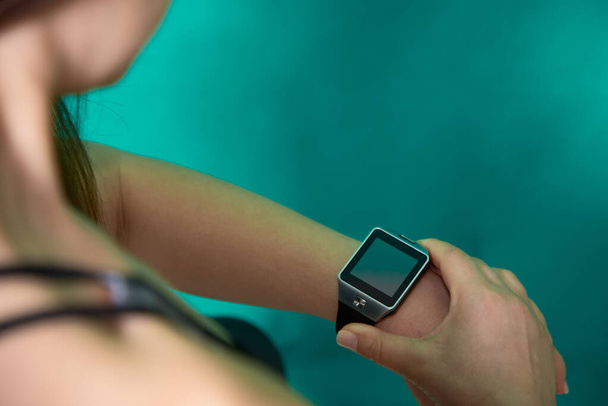Close-up beeld van jonge vrouw controleren van de tijd op smart watch apparaat tijdens indoor oefening. Technologie en fitness. - Foto, afbeelding