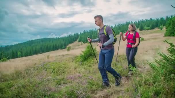 Joven pareja de excursionistas trekking a través de las llanuras boscosas en medio de hermosas montañas en un día nublado. - Metraje, vídeo