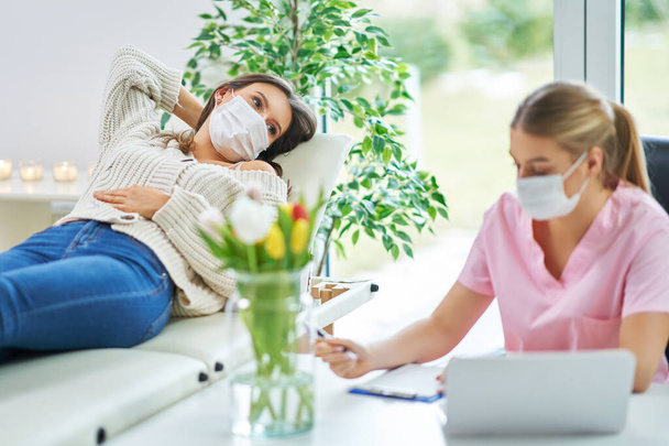 Professional psychiatrist consulting her patient and making notes both in masks - Photo, Image