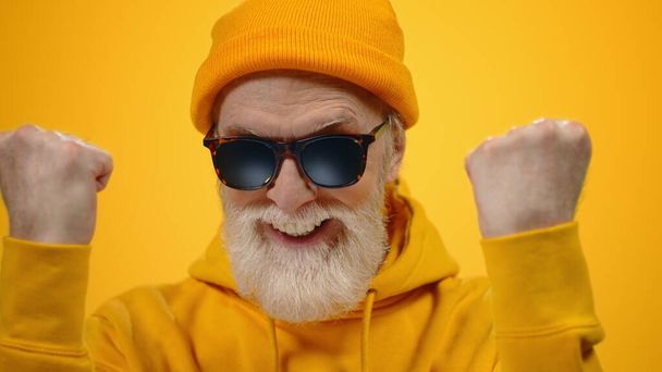 Cheerful aged man enjoying time in studio. Old guy raising hands indoors. - Fotografie, Obrázek