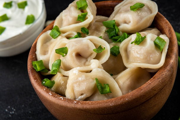 Meat dumplings in wooden bowl with sour cream and green onion on black background. - Φωτογραφία, εικόνα