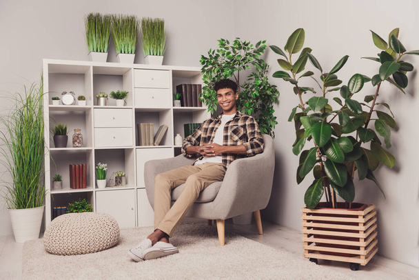 Ganzkörpergröße Foto des Jungen sitzt auf Pause im Sessel zuversichtlich arbeiten im Büro mit grünen Pflanzen - Foto, Bild