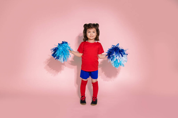 Photo of young girl as cheerleader jumping, kid with blue pom poms - Foto, imagen