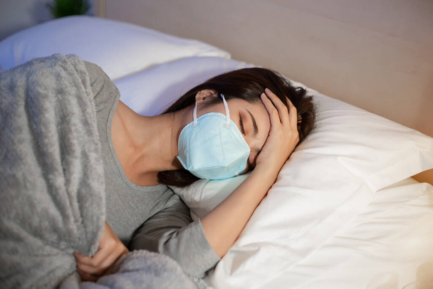 азиатка в маске больная и кашляющая в постели в спальне - Фото, изображение