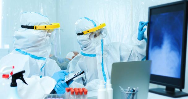 lékaři studující rentgen hrudníku koronavirové plíce pacienta na počítačové obrazovce s izolačním pláštěm nebo ochrannými obleky a chirurgickými obličejovými maskami - Fotografie, Obrázek