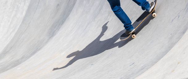 A skater going down a ramp with only his legs and shadow visible - shadow of a skater balancing himself with his arms spread - Фото, изображение