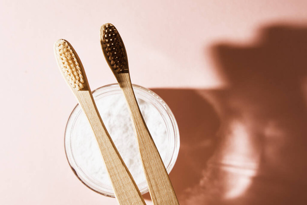 Dwie bambusowe szczoteczki do zębów i proszek do zębów na różowym tle - Zdjęcie, obraz