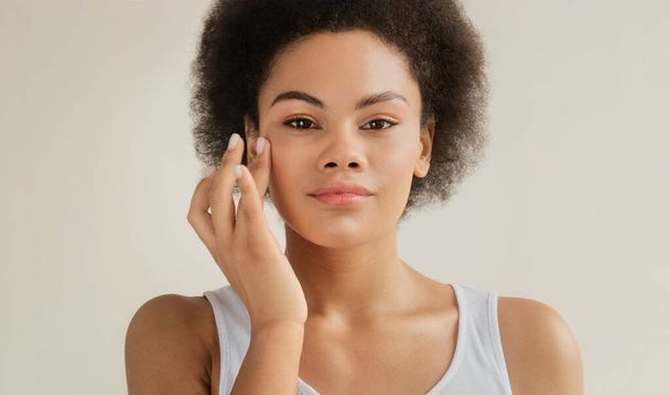 黒アフリカ系アメリカ人女性適用保湿クリーム上の彼女の顔毎日の美しさ製品のためのスキンケア化粧品ルーチン,白の背景にカメラを見て. - 写真・画像