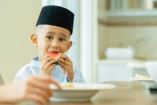 Eid Mubarak momento de celebração, menino comendo frutas. Malásia pessoas vestindo pano tradicional - Foto, Imagem