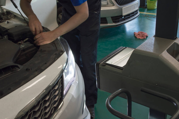 Un electricista ajusta la luz del faro izquierdo de un coche blanco usando un dispositivo en el taller de reparación de automóviles. Vista superior. - Foto, imagen