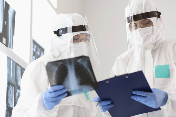 Zwei Ärzte in Schutzanzügen und Masken untersuchen Röntgenbilder - Foto, Bild