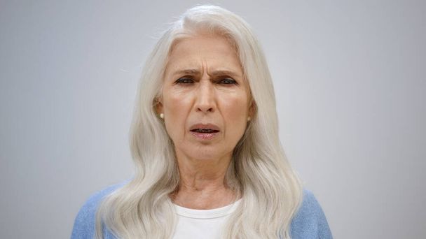 Зрелая женщина закрывает лицо в студии. Серьёзная пожилая леди чихает в помещении. - Фото, изображение