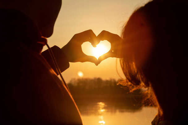 Coppia formato un cuore con le mani sullo sfondo di un tramonto soleggiato. - Foto, immagini
