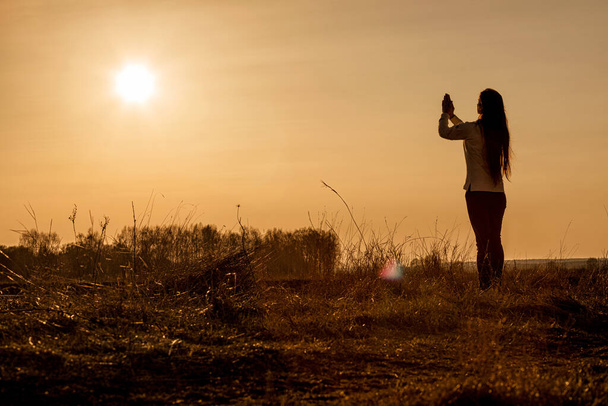 Frau betet vor dem Hintergrund eines sonnigen Sonnenuntergangs mit erhobenen Händen. - Foto, Bild