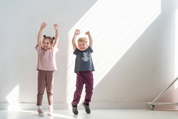 Little happy boy and girl in fashionable clothes smile, pose and jump on the background white wall of the studio. the concept of advertising children's clothing, emotional children, dynamic image - Фото, изображение