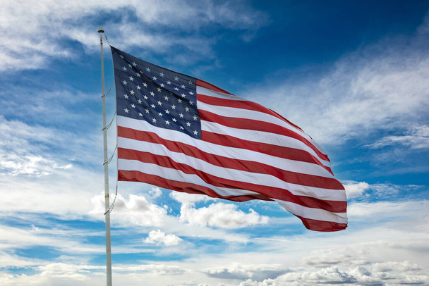 United States of America flag on a pole waving against blue cloudy sky background. USA sign symbol.  - Photo, Image