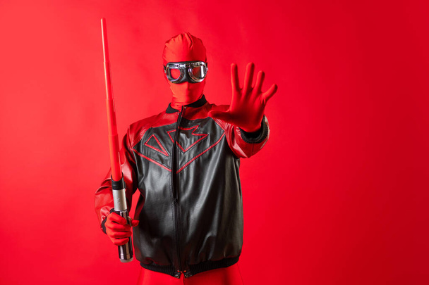 Funny super hero in a red leotard and protective glasses uses a toy sword. - Foto, Imagem