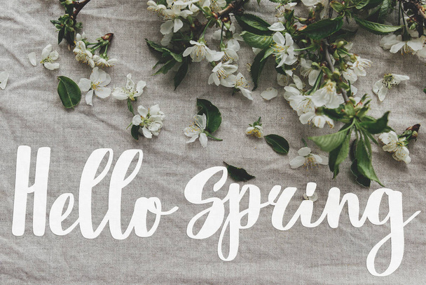 Hello spring. Hello spring text and spring flowers, cherry blossoms, petals, leaves on linen cloth. Handwritten lettering. Springtime. Stylish floral greeting card - Photo, image