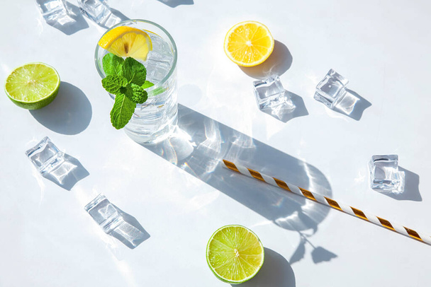 Lemon and mint cocktail or lemonade on a textured stone background, top view. A glass with a drink with a hard shadow from the sunlight. Summer composition. - 写真・画像
