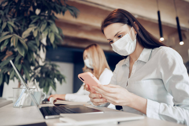 Two female colleagues working in office together wearing medical masks - Foto, afbeelding