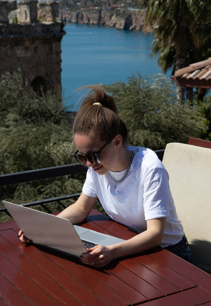 Доросла жінка працює зі своїм ноутбуком на відкритому повітрі в кафе під відкритим небом біля моря
. - Фото, зображення