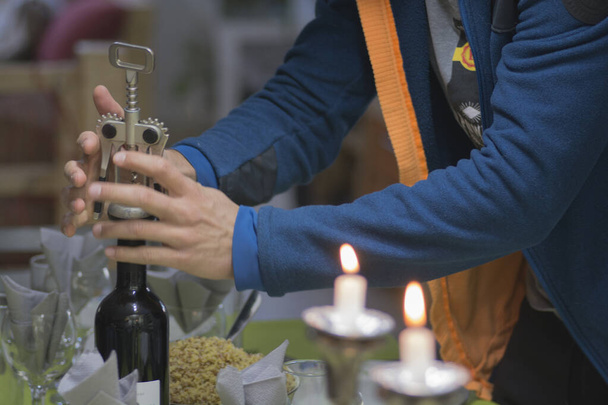 El hombre abre una botella de vino tinto, usando un sacacorchos, durante una cena  - Foto, imagen