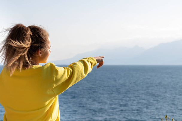 Egy csinos felnőtt nő áll a tenger mellett, és ujjal mutogat a távolba. Visszapillantás. - Fotó, kép