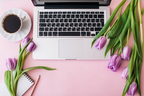 Workspace with laptop, tulip flowers, cup of coffee on pink background. Home office desk. Flat lay, top view, copy space for text. Spring concept - Foto, imagen