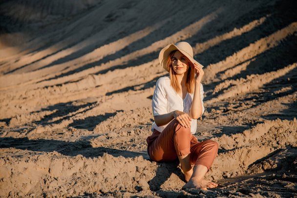 Молодая красивая одинокая женщина с длинными волосами в соломенной шляпе. Одинокая девушка спускается по песчаным дюнам. Летний поэт моды на открытом воздухе. - Фото, изображение