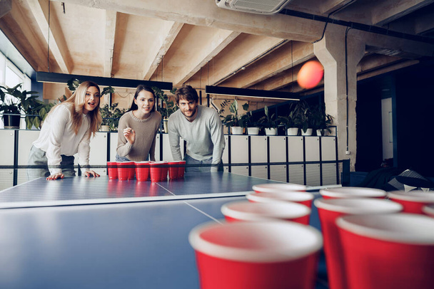 Young people coworkers playing beer pong in modern office - Фото, изображение