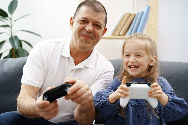 Grandfather and granddaughter playing video games at home. - Fotoğraf, Görsel