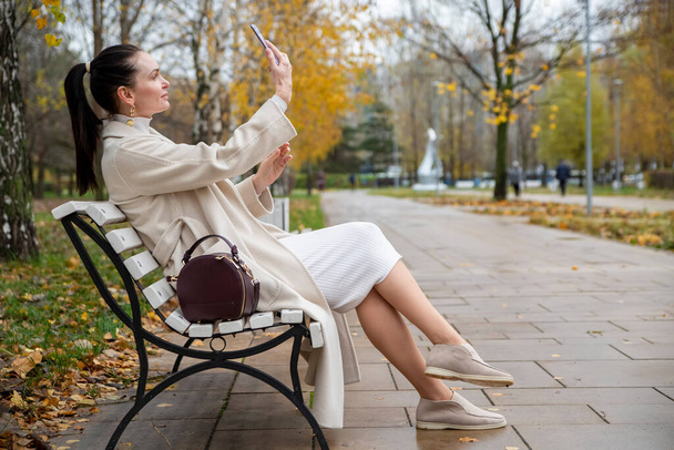 hermosa mujer se sienta en un banco en el parque.. mujer de mediana edad tomando una selfie en el teléfono en el parque - Foto, imagen