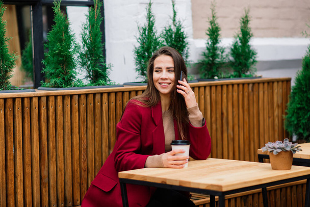 Красивая азиатка пьет кофе в кафе, улыбается, разговаривает по телефону - Фото, изображение