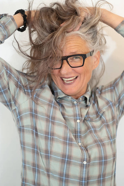 Portrait of an older woman, artist, in her fifties with grey hair and black glasses, her hands tearing her hair and is happy about her success. - Photo, Image