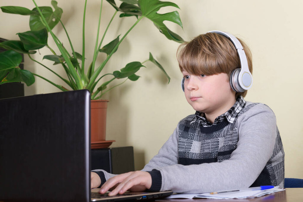 Kulaklık takan güzel çocuk evde dolaşmak için dizüstü bilgisayar ve internet kullanıyor. Evde eğitim, uzak öğrenim - Fotoğraf, Görsel
