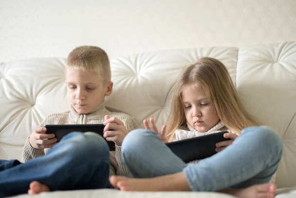 Two little children boy and girl holding tablet and watching cartoons at home. Brother and sister having fun with digital device sitting on couch. - Foto, imagen