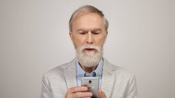 Senior man scrolling on cellphone in studio. Surprised guy using phone indoors. - Foto, afbeelding