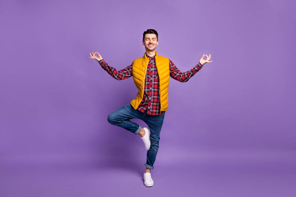 Full length photo of cute sporty young man wear yellow sleeveless jacket practicing yoga isolated violet color background - Фото, зображення