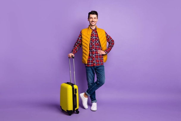 Full length photo of handsome man wear yellow sleeveless jacket holding suitcase arm hand waist isolated violet color background - Foto, Imagem