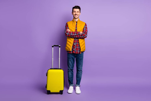 Full length photo of positive confident young guy dressed yellow vest hands arms crossed luggage isolated purple color background - Фото, изображение