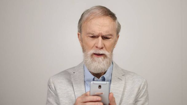 Hombre mayor frustrado leyendo mensajes por teléfono. Tipo molesto buscando teléfono celular. - Foto, imagen