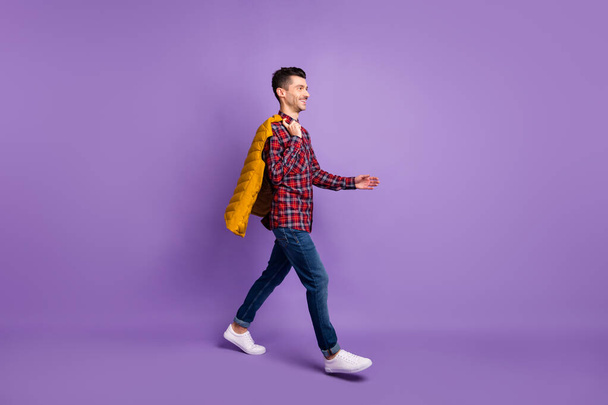 Pleine longueur photo de l'homme porter chemise à carreaux marche tenant dos veste sans manches regardant vide espace isolé couleur violette fond - Photo, image