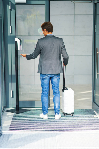 Businessman entering building using hand sanitizer due to covid-19 - 写真・画像