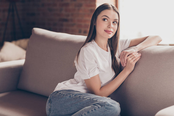 Photo of sweet thoughtful young lady wear white t-shirt sitting sofa smiling having rest indoors house room - Foto, immagini