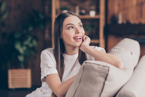 Photo of adorable dreamy young woman white t-shirt sitting couch arm cheek looking window smiling indoors apartment room - 写真・画像