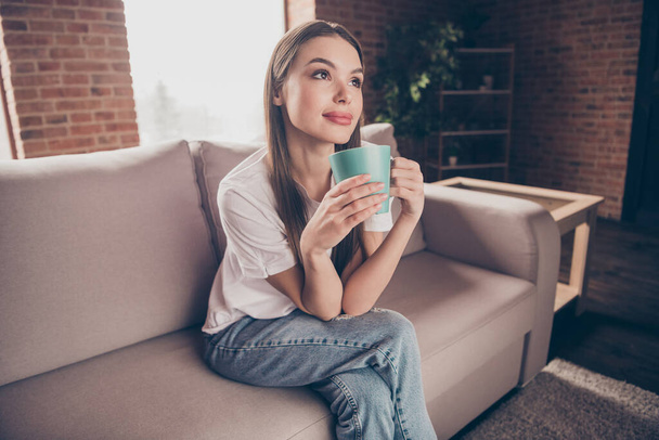 Photo of shiny dreamy young lady wear white t-shirt sitting sofa drinking beverage indoors house room - Foto, Imagem